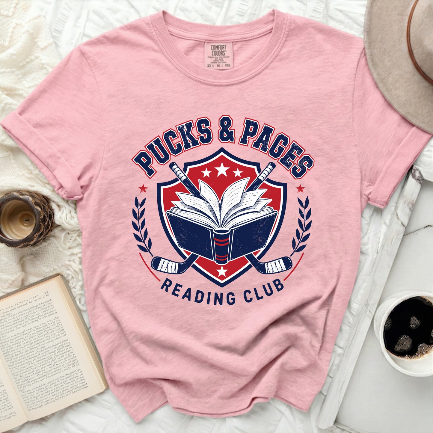 Pink t-shirt with "Pucks & Pages Reading Club" crest design.