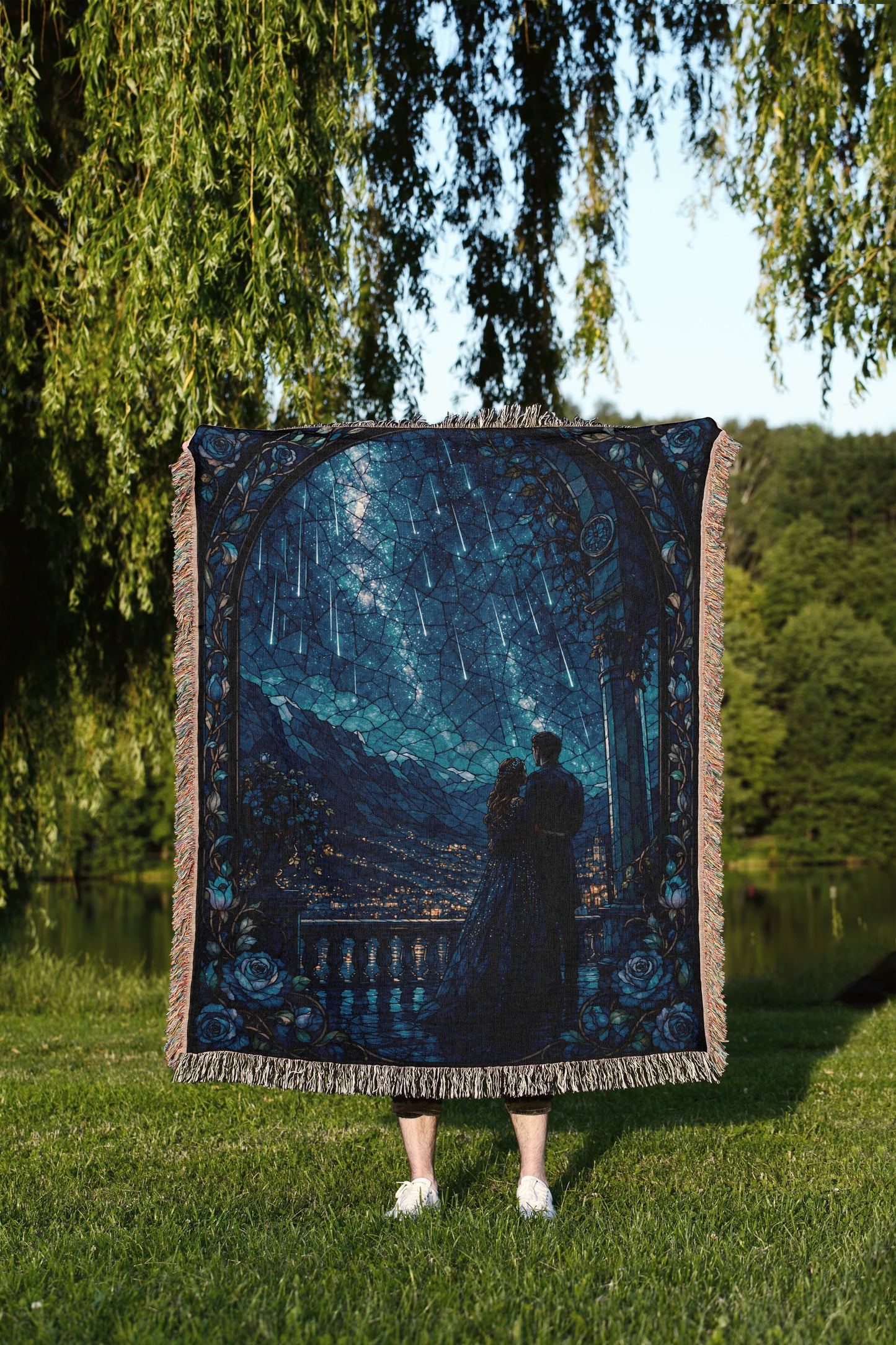 A person stands in a grassy field, holding a large tapestry or blanket that features a night sky scene with falling stars.