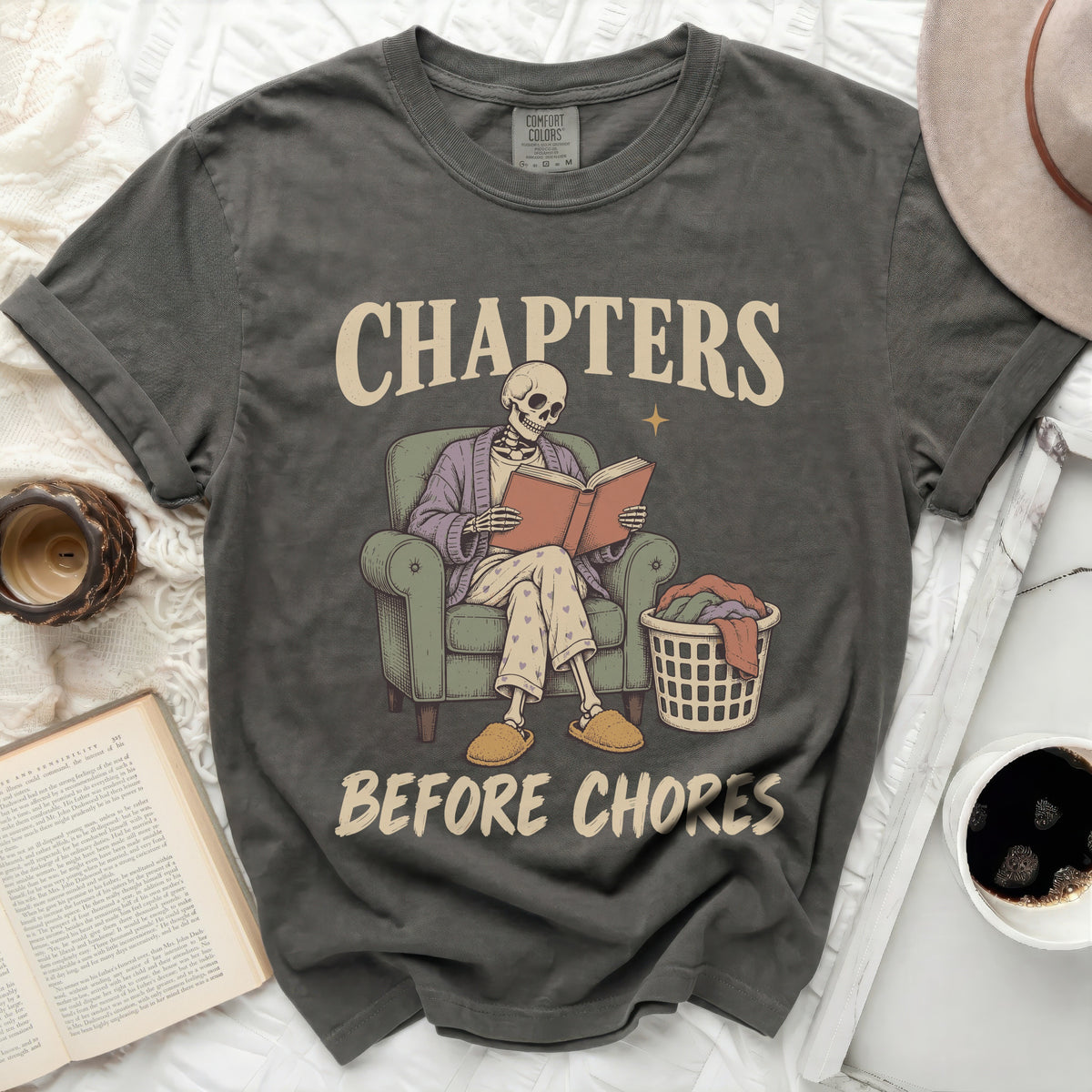 Graphic tee with skeleton reading a book and text "CHAPTERS BEFORE CHORES".