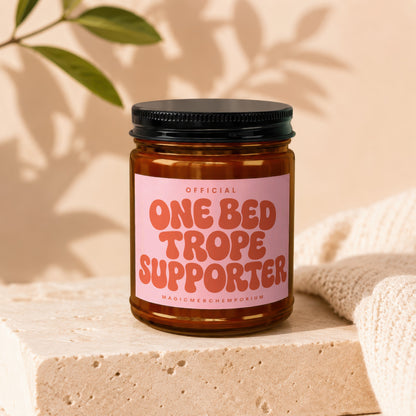 Amber glass candle with pink label reading "Official One Bed Trope Supporter".