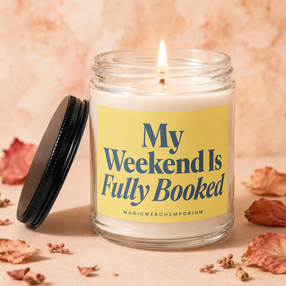 Lit candle in glass jar with yellow label reading "My Weekend Is Fully Booked".