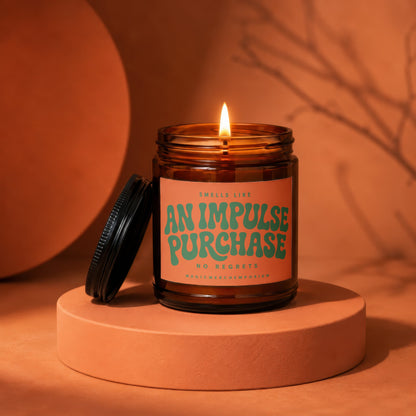 Amber jar candle with lit wick and label reading "Smells like an impulse purchase. No regrets."
