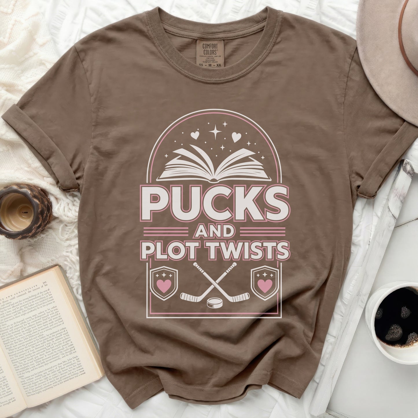 Brown t-shirt with "Pucks and Plot Twists" and crossed hockey sticks graphic.