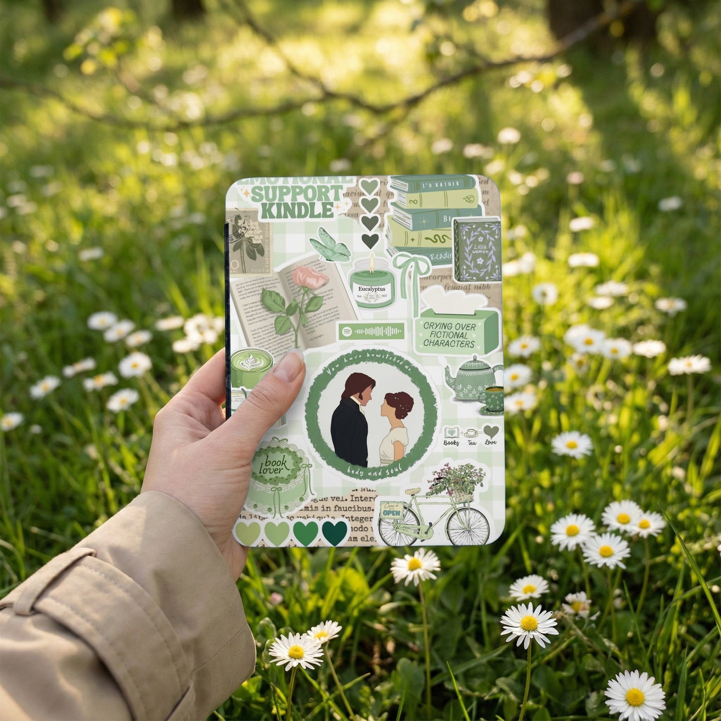 Kindle cover with green book, tea, and floral designs, held in hand.