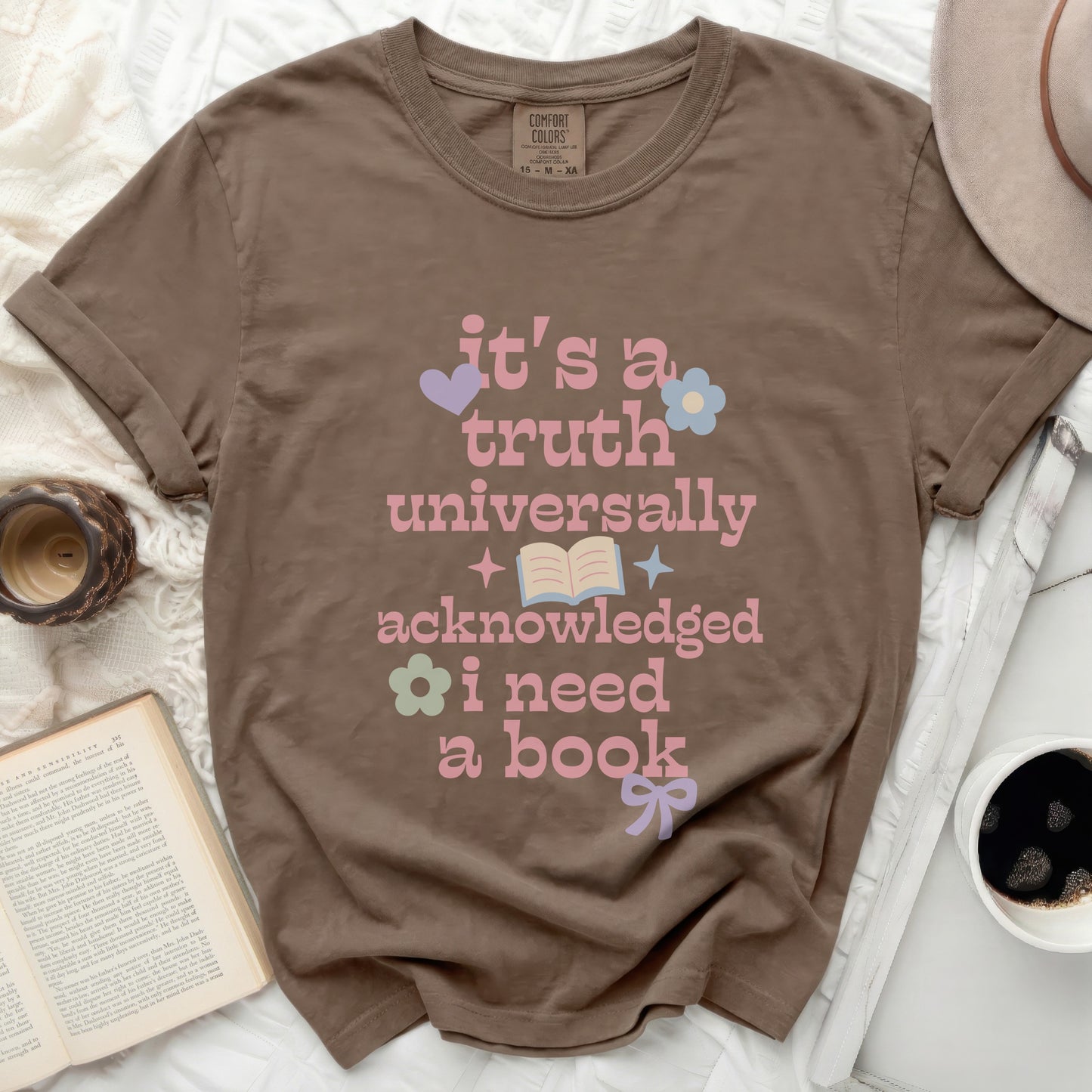 Brown t-shirt with pink text "it's a truth universally acknowledged i need a book"
