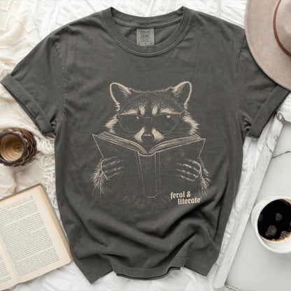 T-shirt with raccoon wearing glasses reading a book, "feral & literate" text.