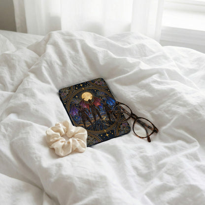 A Kindle case with a fantasy illustration rests on a white bed alongside glasses and a scrunchie.