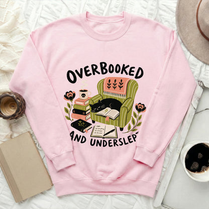 Pink sweatshirt with "Overbooked and Underslept" text and cat in armchair design.
