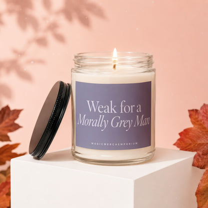 Candle with label "Weak for a Morally Grey Man" on a white cube.