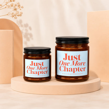 Two amber glass candles with black lids, labeled "Just One More Chapter."