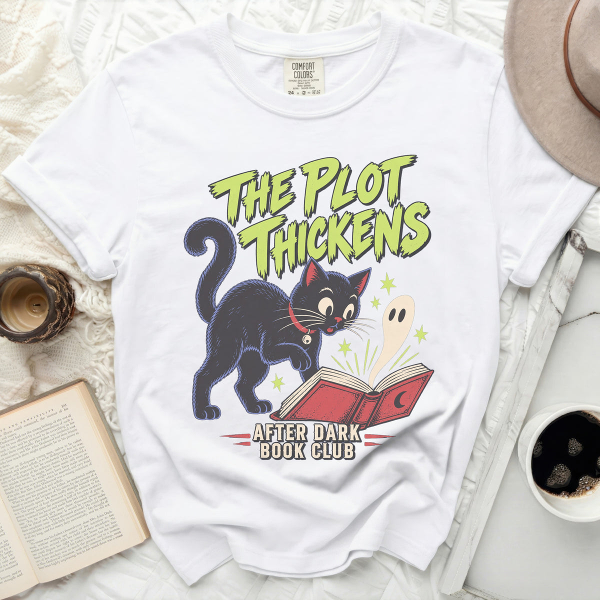White t-shirt with black cat, ghost, and books graphic, saying "The Plot Thickens After Dark Book Club".