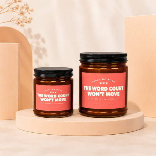 Two amber glass candles with black lids and pink labels that read "The Word Count Won't Move".