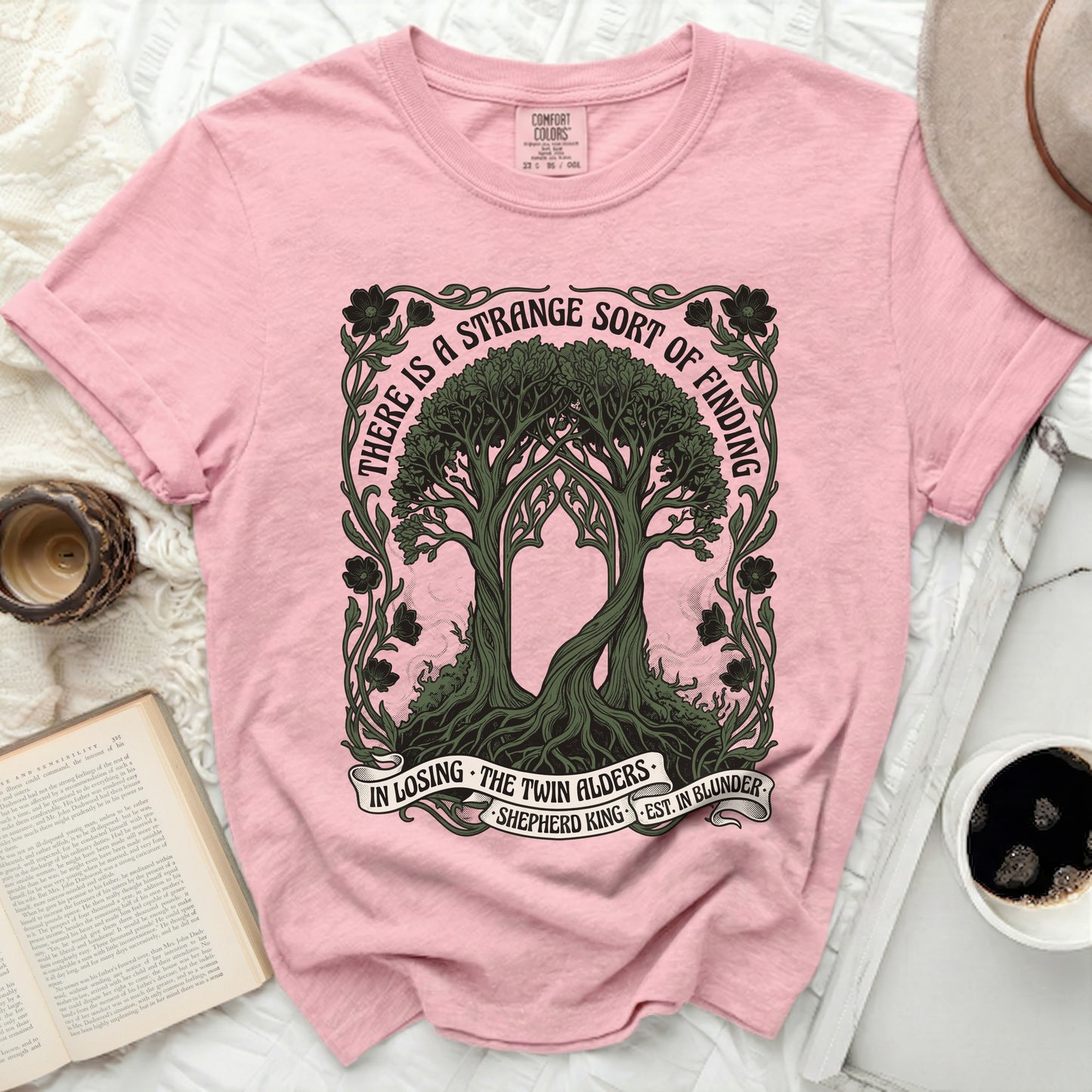 Pink t-shirt with twin trees design and "There is a strange sort of finding" text.