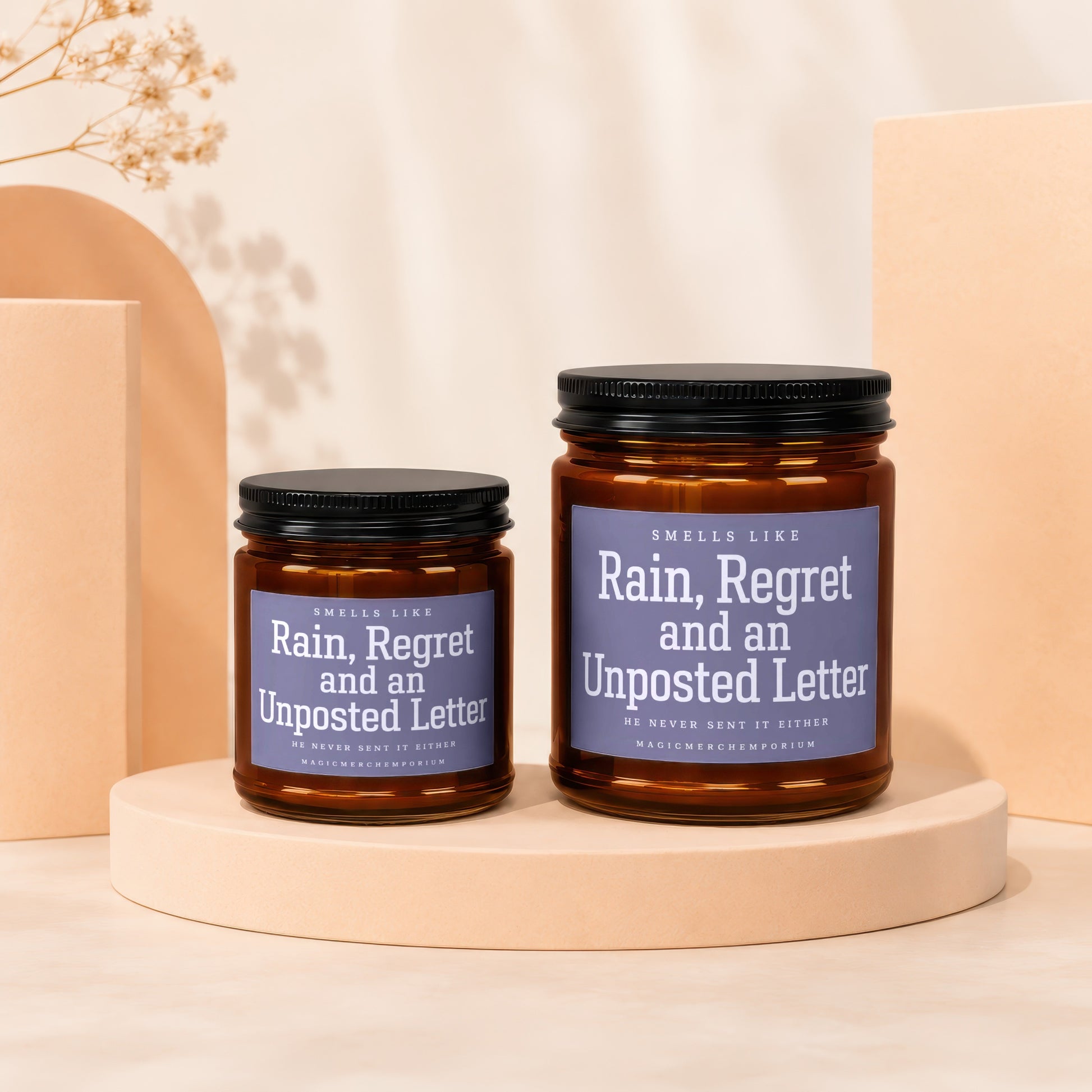 Two amber glass jar candles with black lids branded "Rain, Regret and an Unposted Letter".