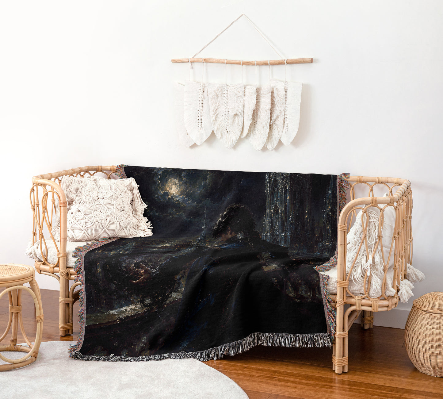a cozy living room with a black and white patterned blanket draped over a wicker bench. The bench is adorned with white pillows and a woven basket is placed nearby. A hanging wall decoration with white feathers adds a touch of elegance to the space.