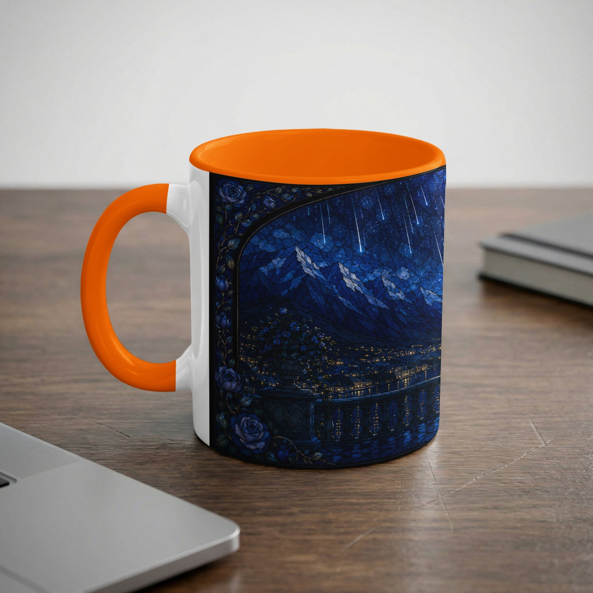 White mug with orange handle, decorated with a starry night cityscape and mountains.