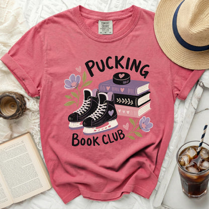Pink t-shirt with ice skates, books, and flowers, featuring "Pucking Book Club" text.