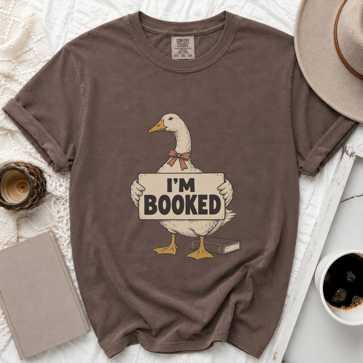 Brown t-shirt with a goose graphic holding a sign that says "I'M BOOKED".