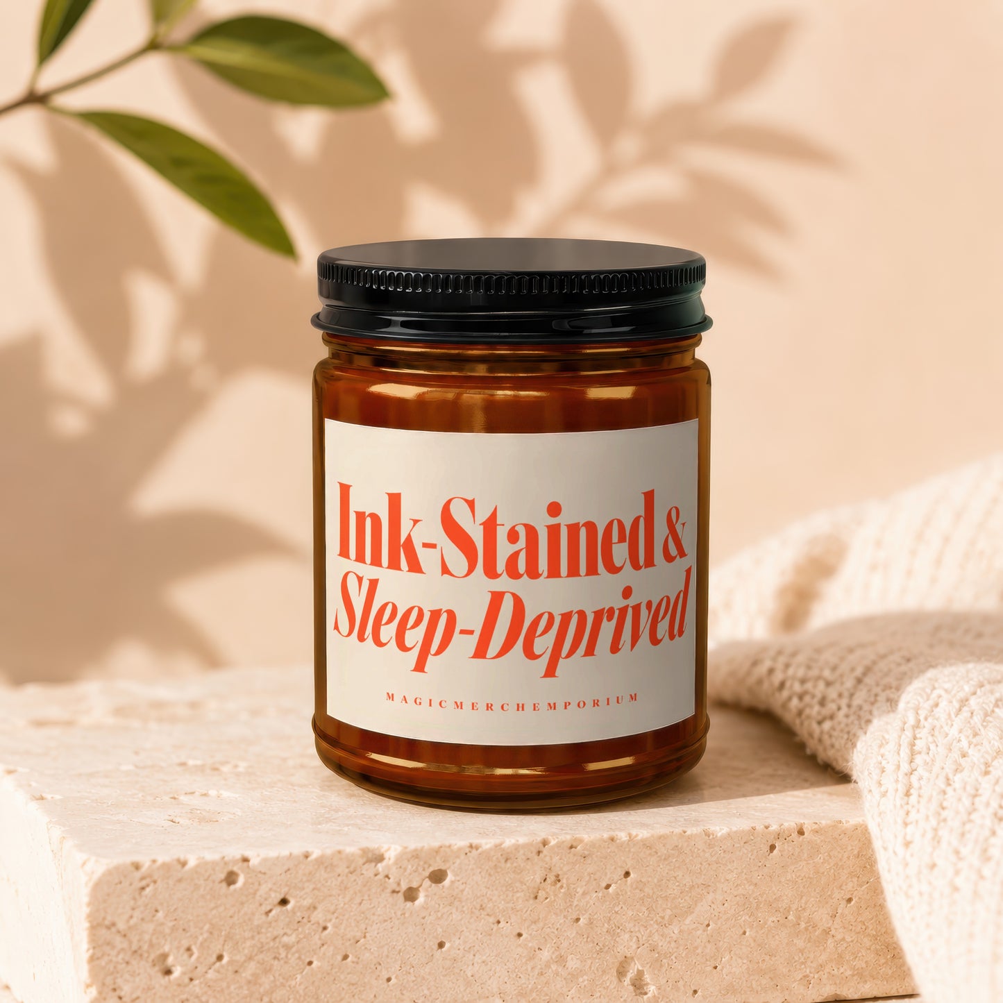 Amber jar candle with label reading "Ink-Stained & Sleep-Deprived MagicMerchEmporium".
