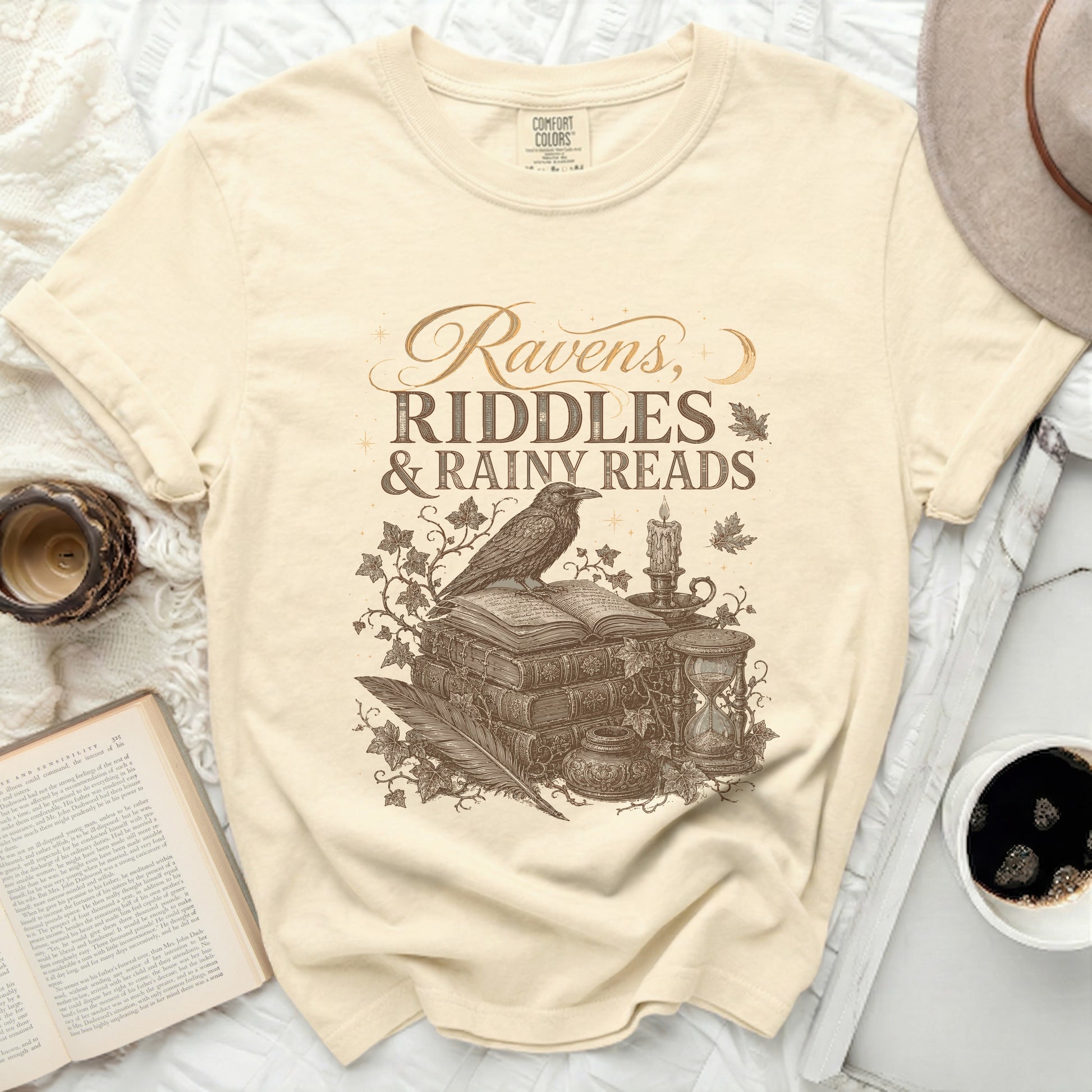 Ravens, Riddles & Rainy Reads graphic on a cream t-shirt.