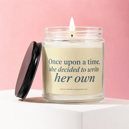 Glass candle with lit wick and black lid, reading "Once upon a time, she decided to write her own".