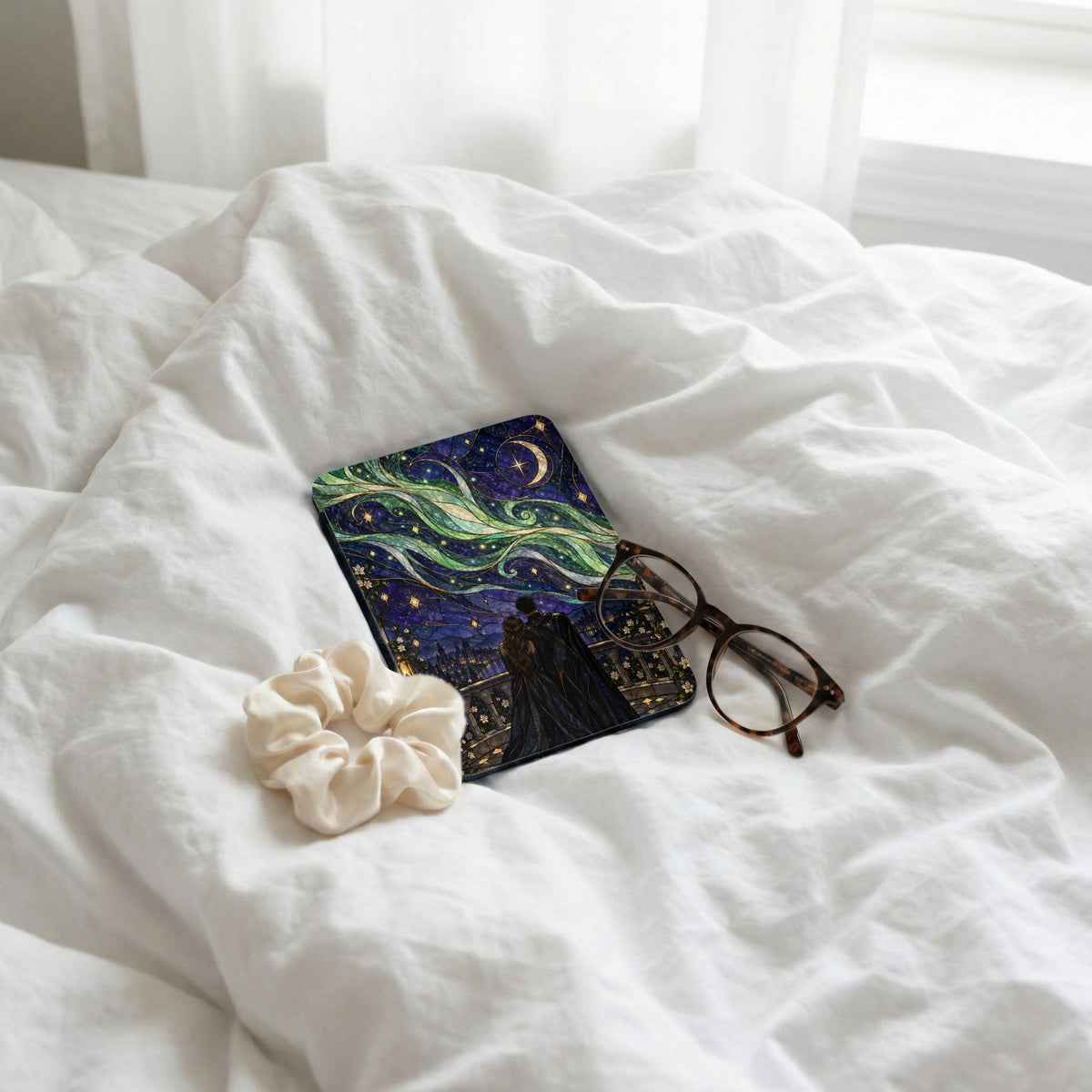 Cover with a starry night design, scrunchie, and glasses on rumpled white sheets.