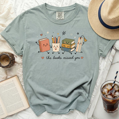 Light green t-shirt with cute cartoon books, pencil cup, and bookmark saying "the books missed you".