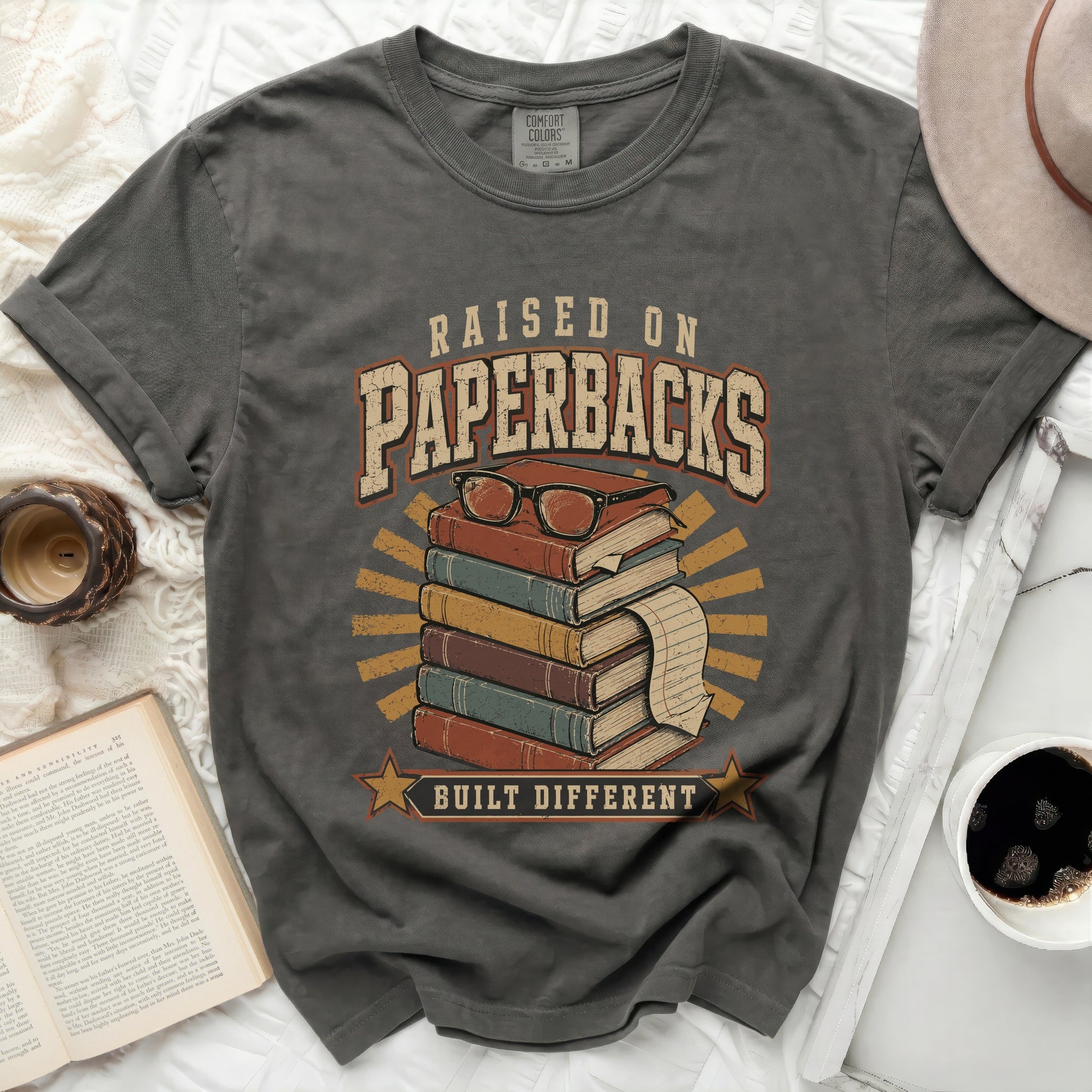 Raised on Paperbacks Built Different t-shirt with stack of books and glasses.