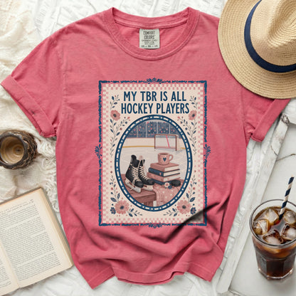 Pink t-shirt with a framed graphic of ice skates, books, and hockey goal.