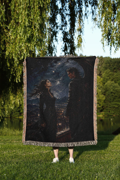 A person is standing in a grassy area, holding a large square blanket that features a painting of a woman and a man.