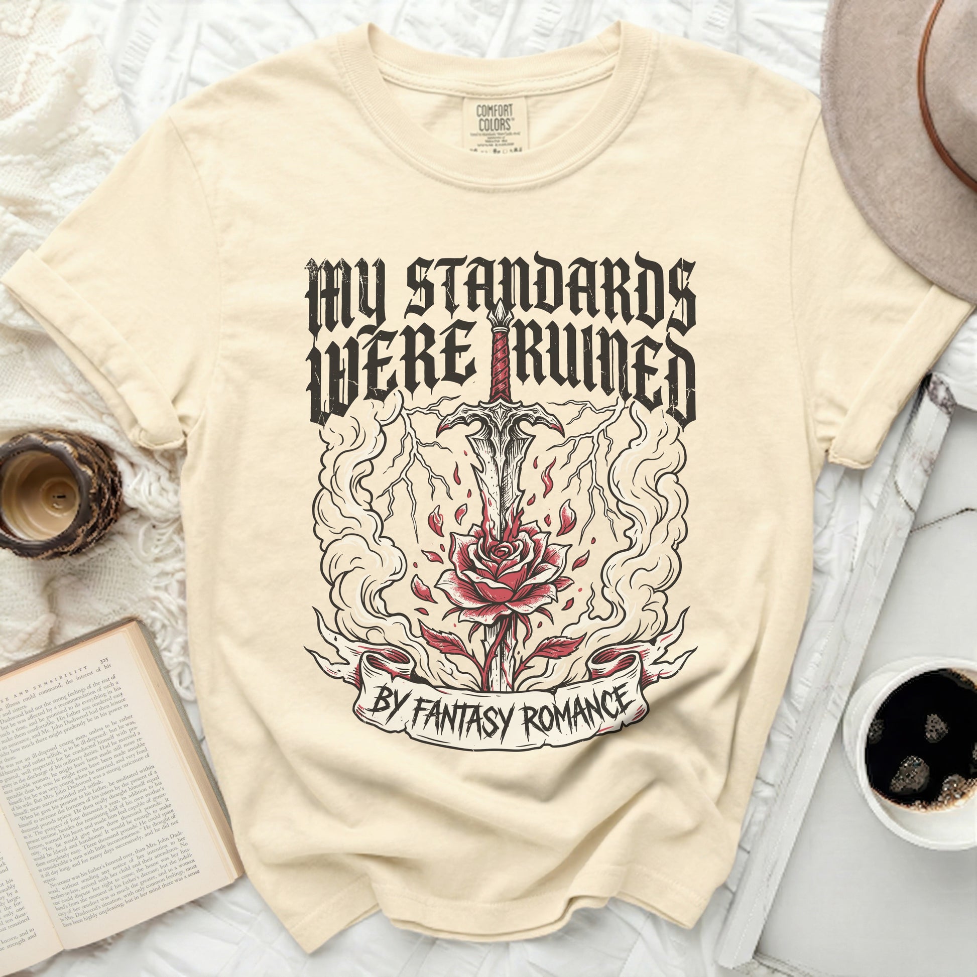 Cream t-shirt with "MY STANDARDS WERE RUINED BY FANTASY ROMANCE" graphic.