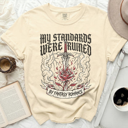 Cream t-shirt with "MY STANDARDS WERE RUINED BY FANTASY ROMANCE" graphic.