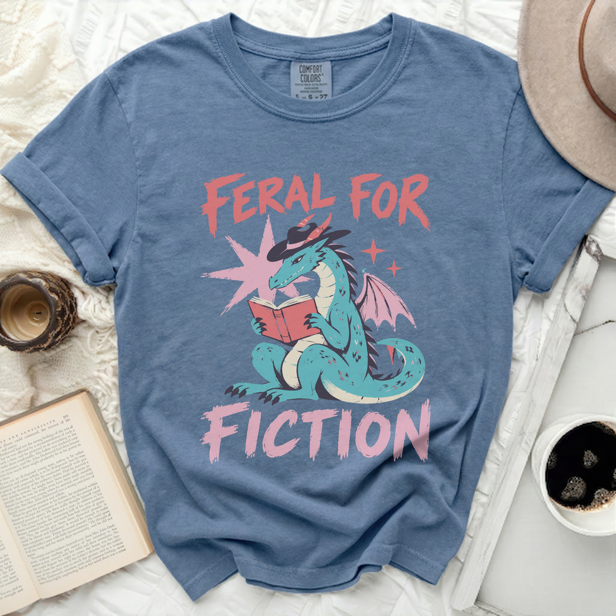 Dragon wearing a hat reading a book with "Feral For Fiction" text.