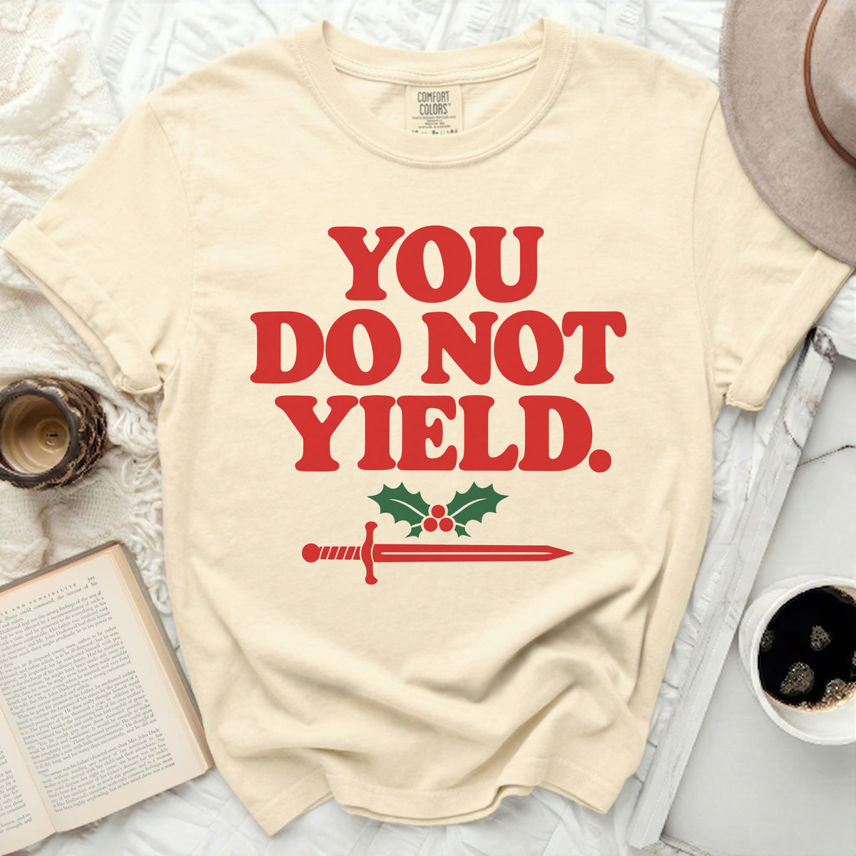 Cream t-shirt with red text "YOU DO NOT YIELD." and a sword and holly graphic.