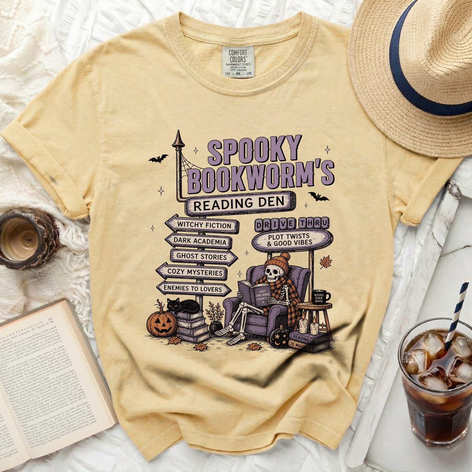 Spooky Bookworm's Reading Den t-shirt with skeleton reading book, pumpkins, and genre signs.
