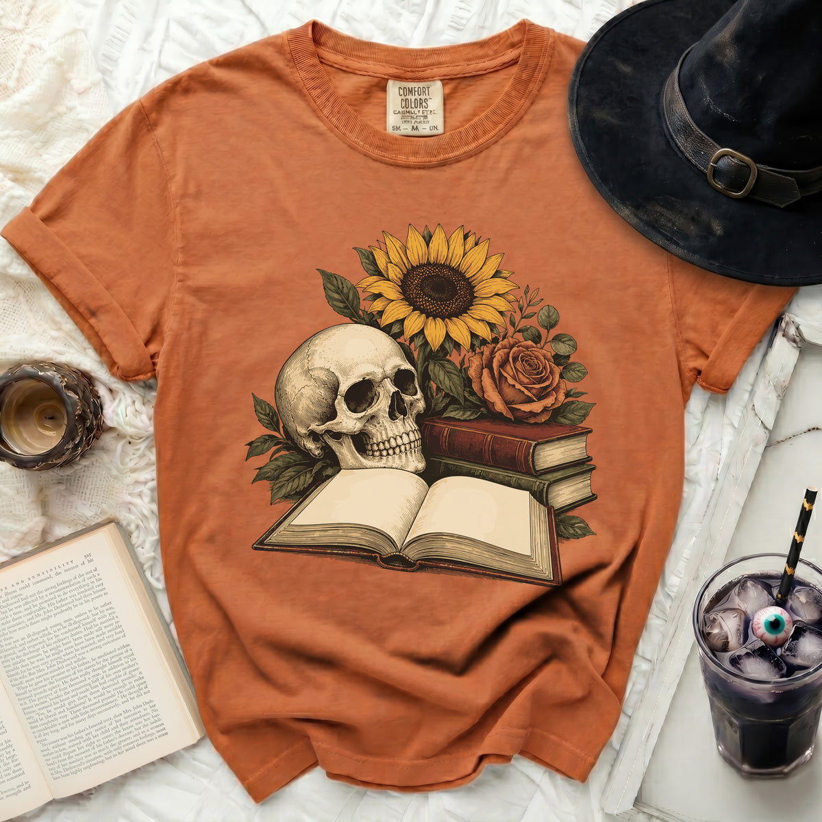 Orange Comfort Colors t-shirt with skull, sunflower, roses, and open books graphic.