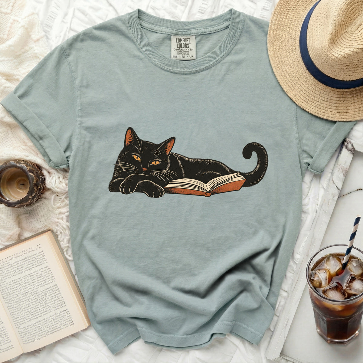 Black cat lounging on an open book, printed on a Comfort Colors t-shirt.