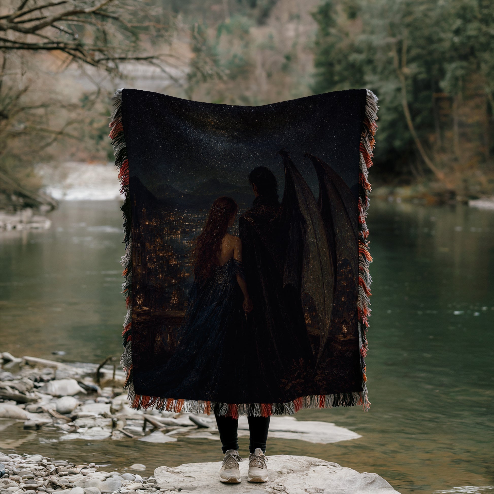 A person stands on a rock, holding a large blanket with a painting of two people on it, partially obscuring their face.