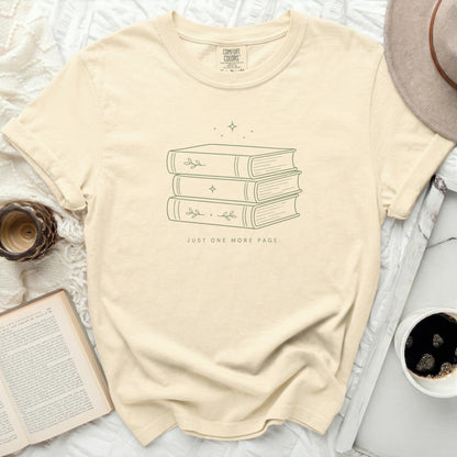Cream t-shirt with stacked books and "JUST ONE MORE PAGE" text.
