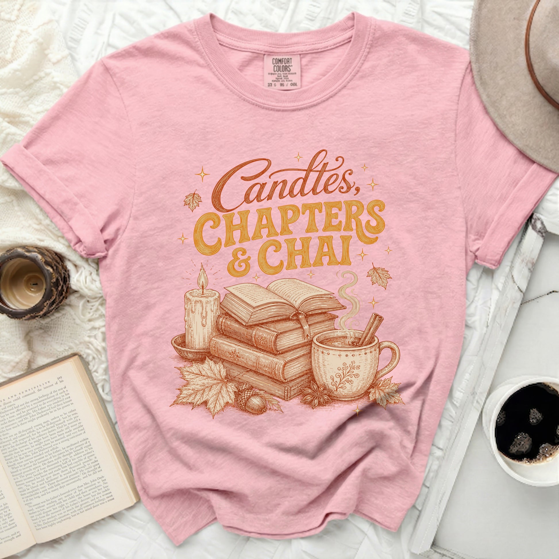 Pink t-shirt with "Candles, Chapters & Chai" graphic and autumn motifs.