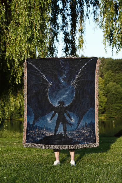 A person is standing in a grassy area, holding a large square blanket with a painting of a winged figure against a night sky background.