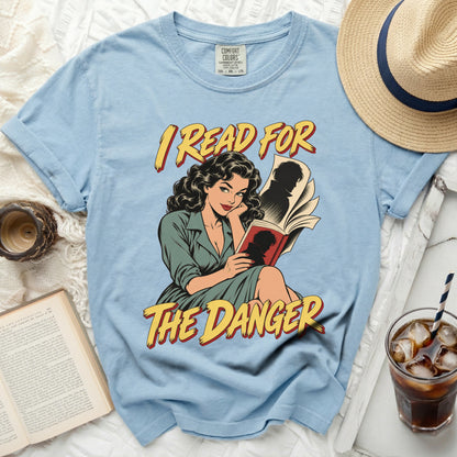 Light blue t-shirt with graphic art of a woman reading a book, text "I READ FOR THE DANGER".