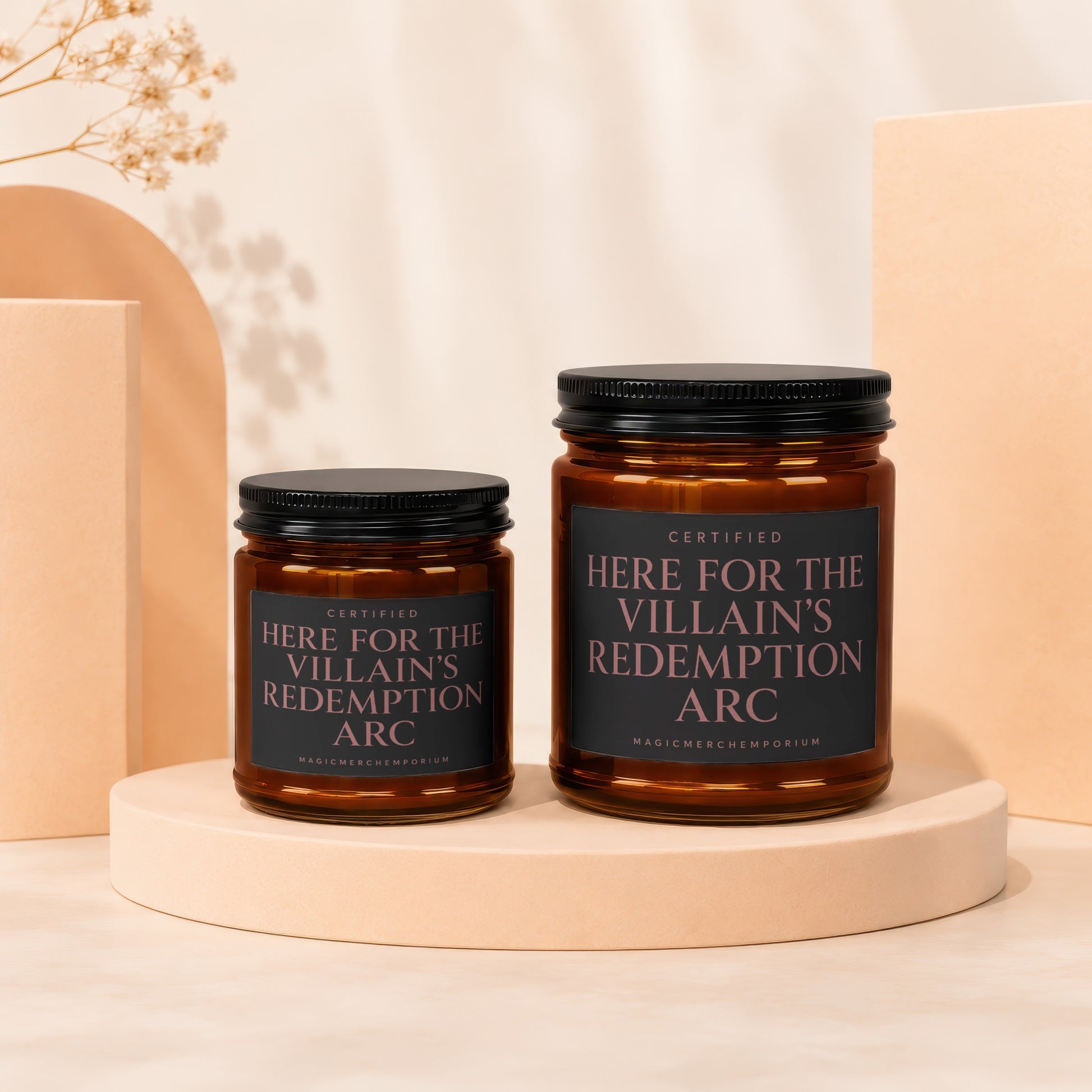 Two amber glass candles with black lids and labels reading "Certified Here For The Villain's Redemption Arc".