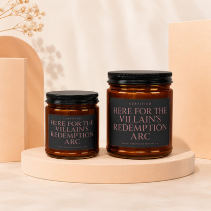 Two amber glass candles with black lids and labels reading "Certified Here For The Villain's Redemption Arc".