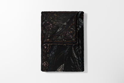 Black blanket with dark floral pattern and winged creature design.