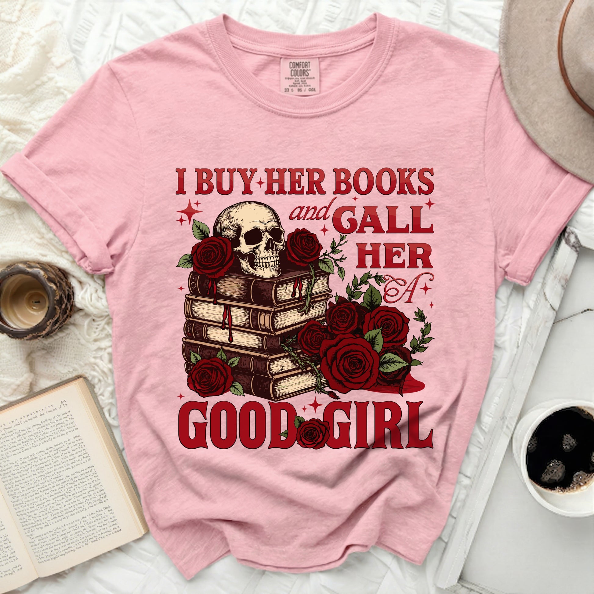 Pink t-shirt with skull, books, and red roses graphic reading "I buy her books and gall her a good girl."