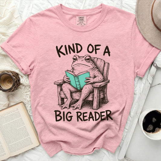Pink t-shirt with a frog reading a book, text "KIND OF A BIG READER".