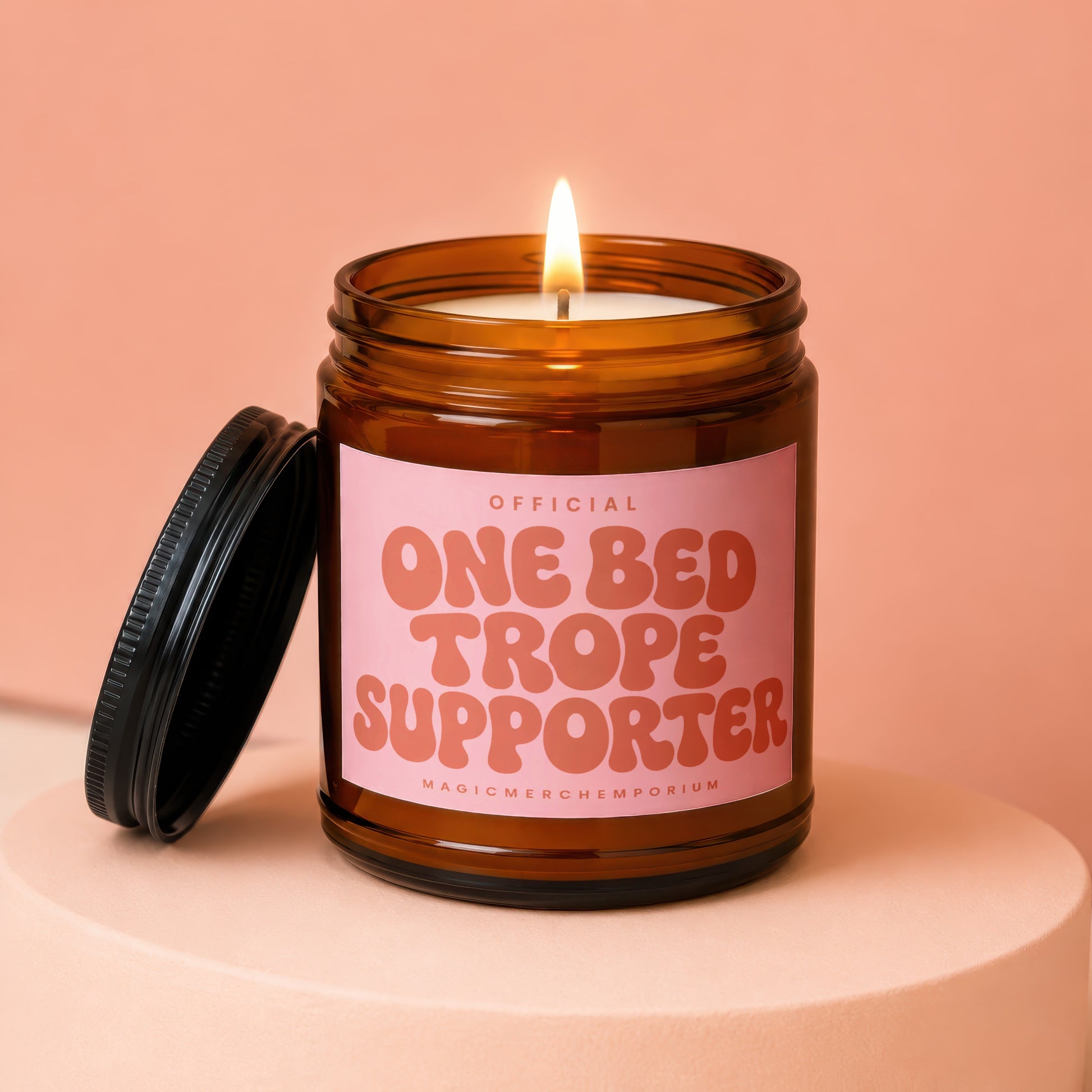 Amber glass candle with pink label that reads "Official One Bed Trope Supporter"
