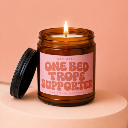 Amber glass candle with pink label that reads "Official One Bed Trope Supporter"