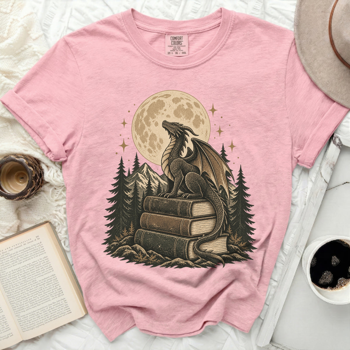 Pink t-shirt with dragon on books graphic under a moon and stars.